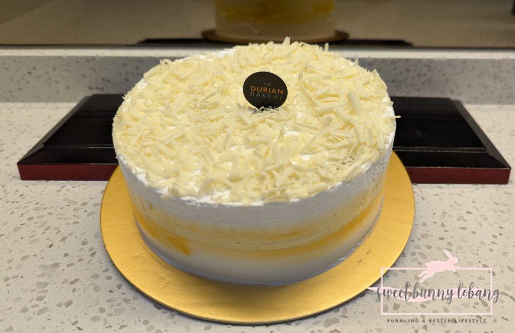 A white cake adorned with The Durian Bakery's black and white logo.