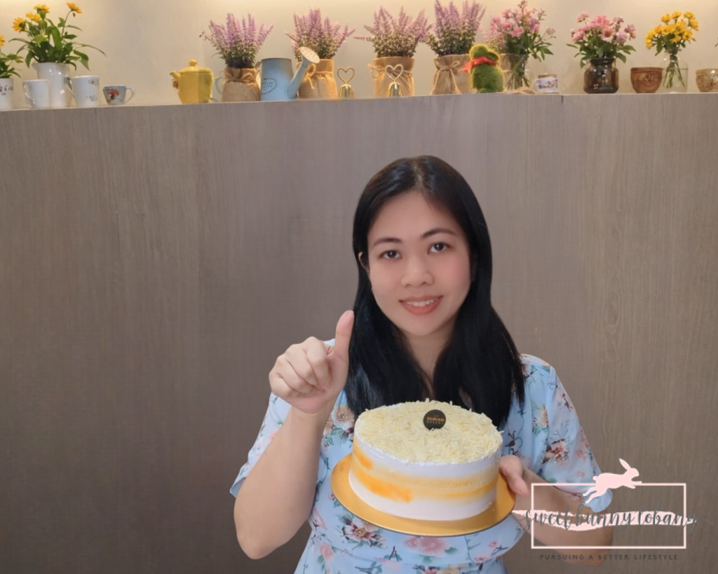 A woman proudly displays a Classic Mao Shan Wang Durian Cake while giving a thumbs up, indicating her approval.