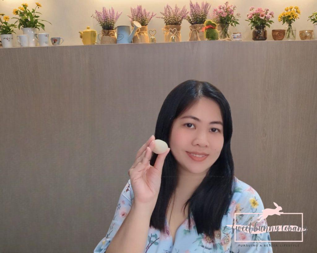 A woman holds a white Snowy D24 Durian Mochi ball in front of her face, showcasing the dessert from the durian bakery.