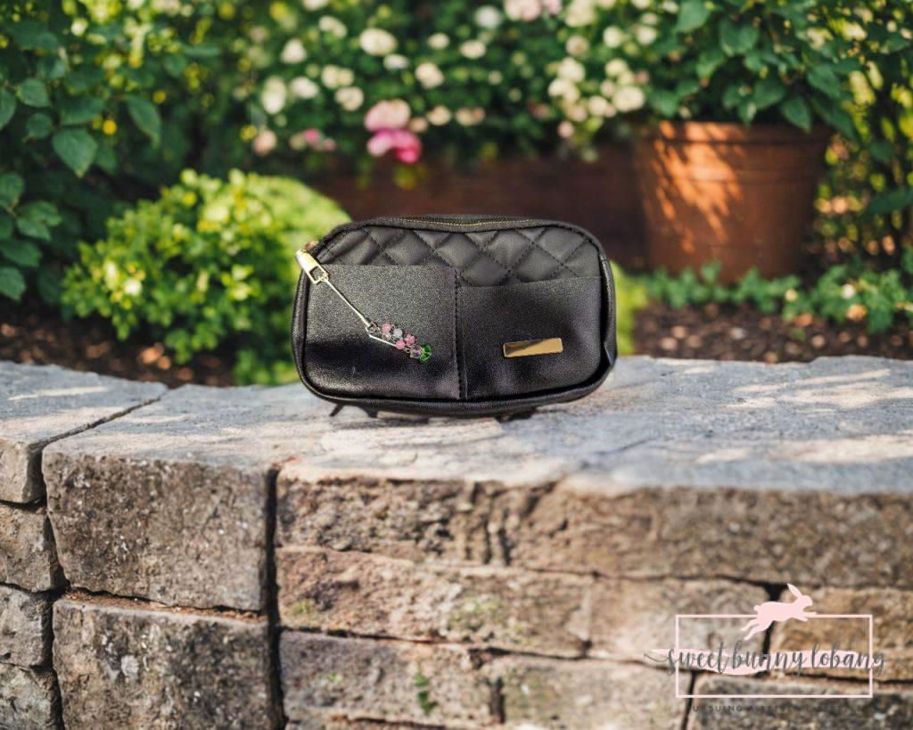 A black purse rests on a stone wall, featuring a charm shaped like a SIM card pin.