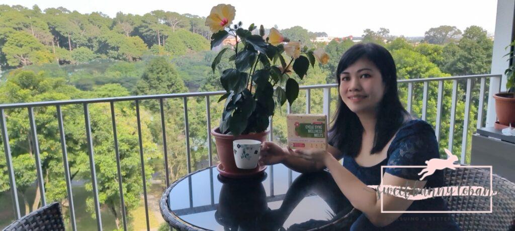 Nano Singapore Cycle Sync Wellness Melts Review* 2 A woman sitting on a balcony, enjoying the view while holding a package of Nano Singapore Cycle Sync Wellness Melts.