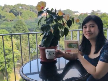 A woman sitting on a balcony, enjoying the view while holding a package of Nano Singapore Cycle Sync Wellness Melts.