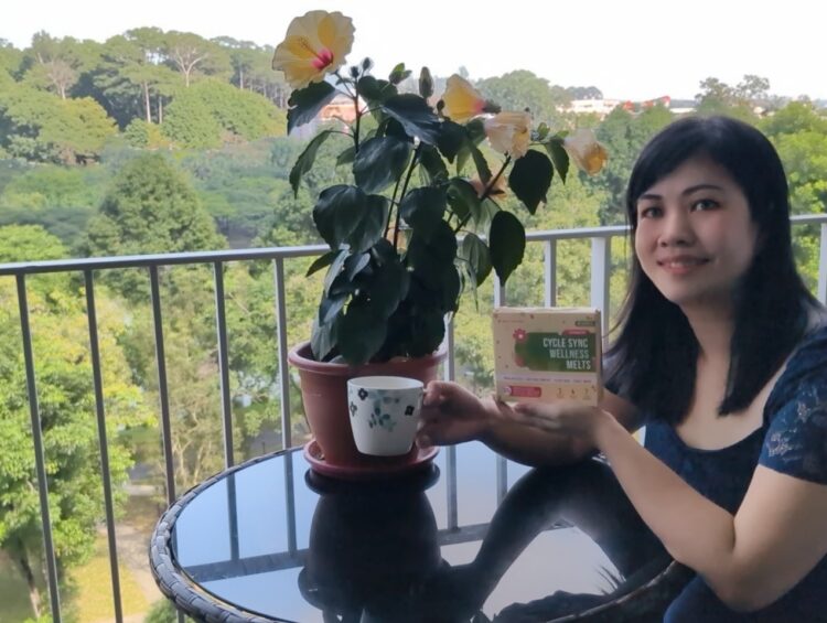 Nano Singapore Cycle Sync Wellness Melts Review* 1 A woman sitting on a balcony, enjoying the view while holding a package of Nano Singapore Cycle Sync Wellness Melts.
