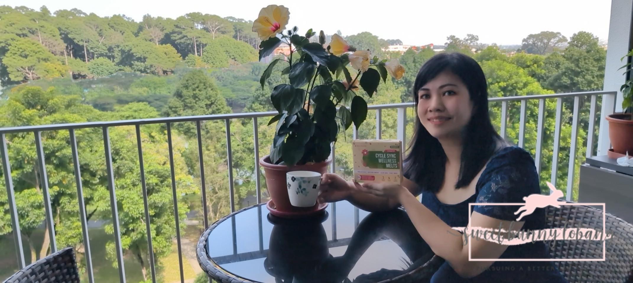 A woman sitting on a balcony, enjoying the view while holding a package of Nano Singapore Cycle Sync Wellness Melts.